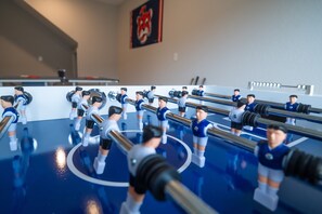 Ein Kicker mit mehreren Spielern und Spielstangen, vor einem blauen Boden mit weißer Begrenzung.