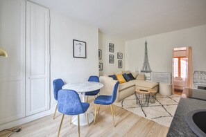 Olohuoneessa on pyöreä pöytä, siniset tuolit, vaaleanbeige sohva koristetyynyineen sekä pieni pyöreä sohvapöytä. Seinällä on kehystettyjä kuvia ja suuri Eiffel-tornin kuva.