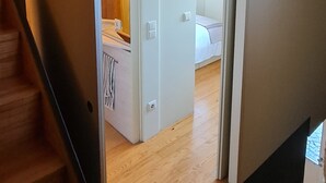 Un couloir menant à une chambre avec un lit, une salle de bain avec une douche et un escalier.