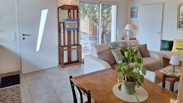 Een gezellige woonkamer met houten plafond, een bank, een eettafel met stoelen en uitzicht op het buitenlands via een glazen deur.