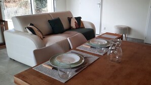 Een eetgedeelte met een houten tafel gedekt voor twee personen, een witte bank met kussens en uitzicht op de omgeving.