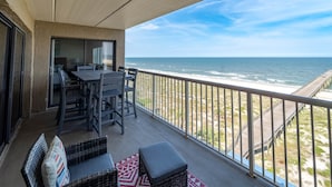 A balcony with a view of the ocean, furnished with a table and chairs, and a small seating area. - 779 Amelia by the Sea, Amelia by the Sea 3 Bedroom! Fishing Pier! Oceanfront! (Fernandina Beach)