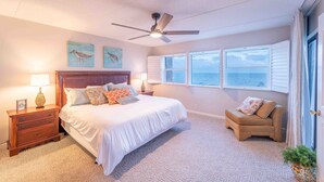A bedroom with a bed, a nightstand, a chair, a ceiling fan, and a window with a view of the ocean. - 779 Amelia by the Sea, Amelia by the Sea 3 Bedroom! Fishing Pier! Oceanfront! (Fernandina Beach)