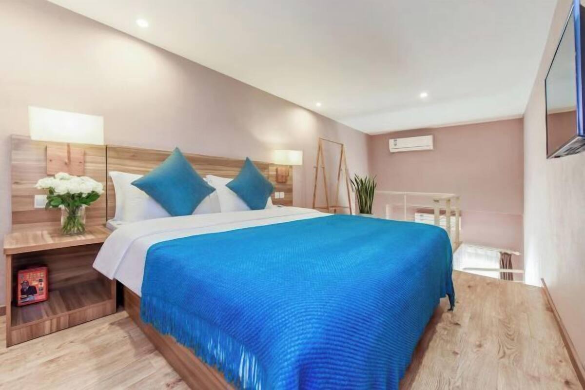A modern hotel room with a large bed, bedside lamps, a nightstand, and a mirror.