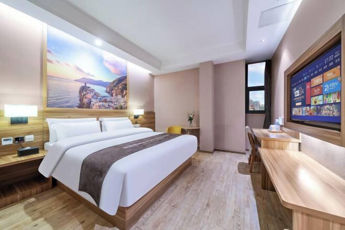A hotel room with a bed, bedside tables, a desk, a chair, a TV, and a large painting on the wall.