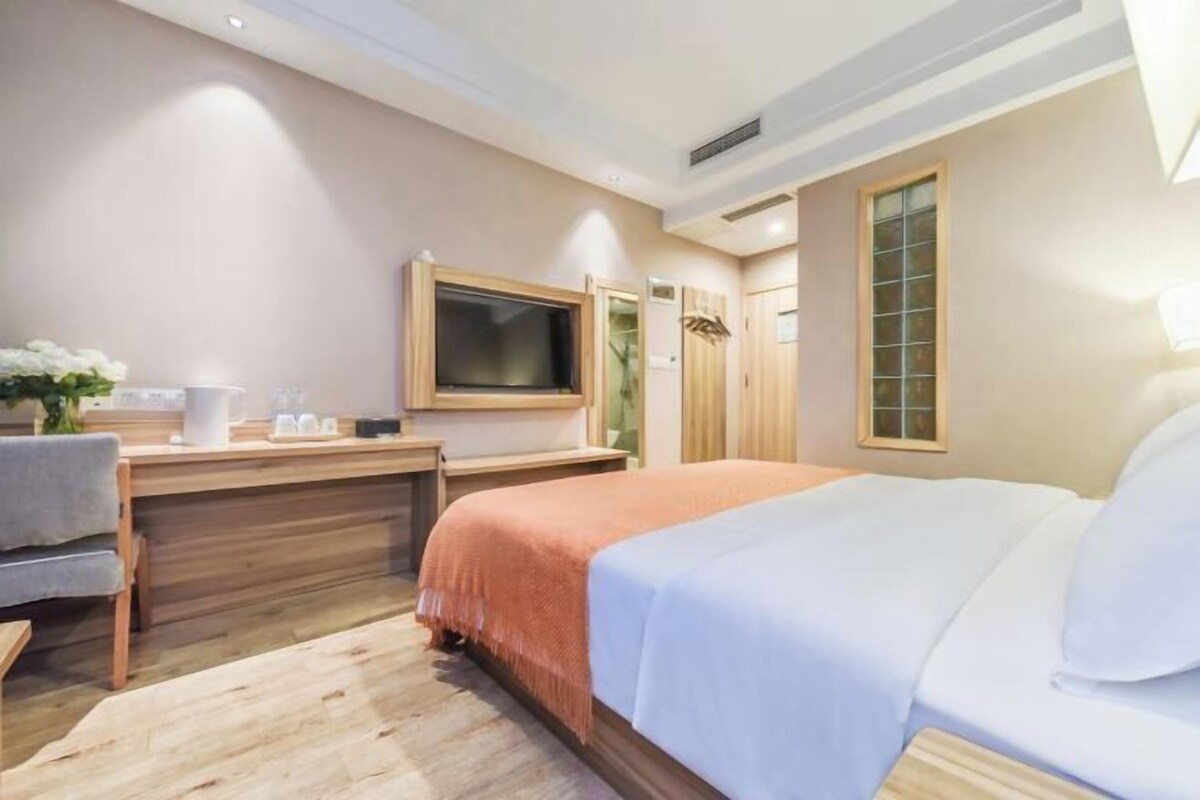 A hotel room with a bed, a desk, a TV, and a window.