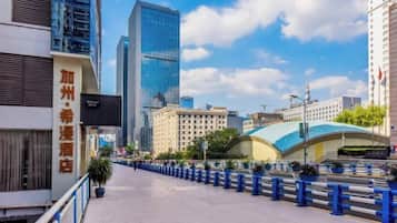Una calle urbana con edificios modernos, cielo despejado y una barandilla azul a lo largo de la acera.
