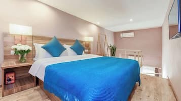 Una habitación de hotel moderna con una cama grande, cabecero de madera, mesitas de noche y un televisor.