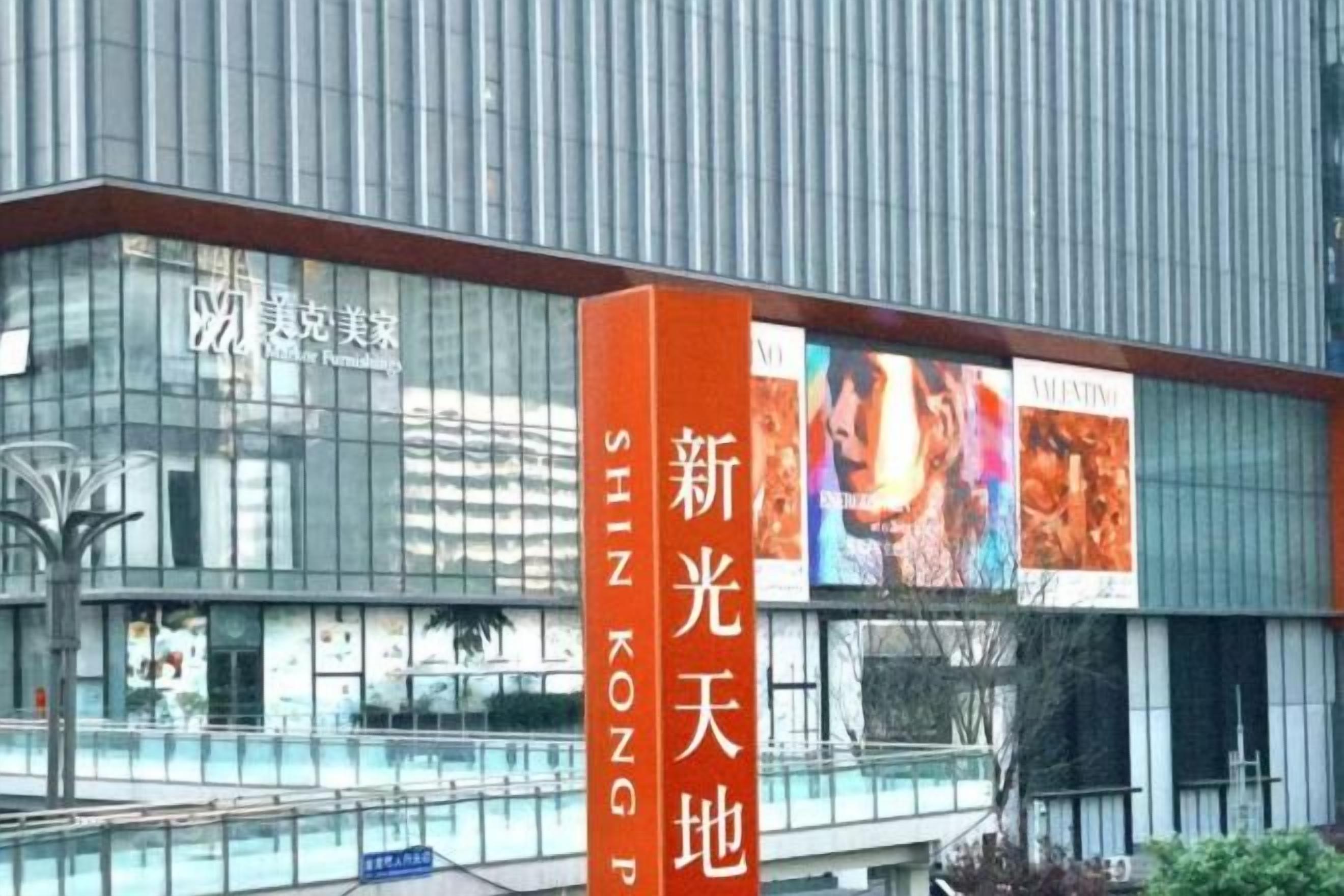 Een modern gebouw met een glazen gevel, een opvallend oranje bord met Chinese karakters, en een reclamebord erboven.