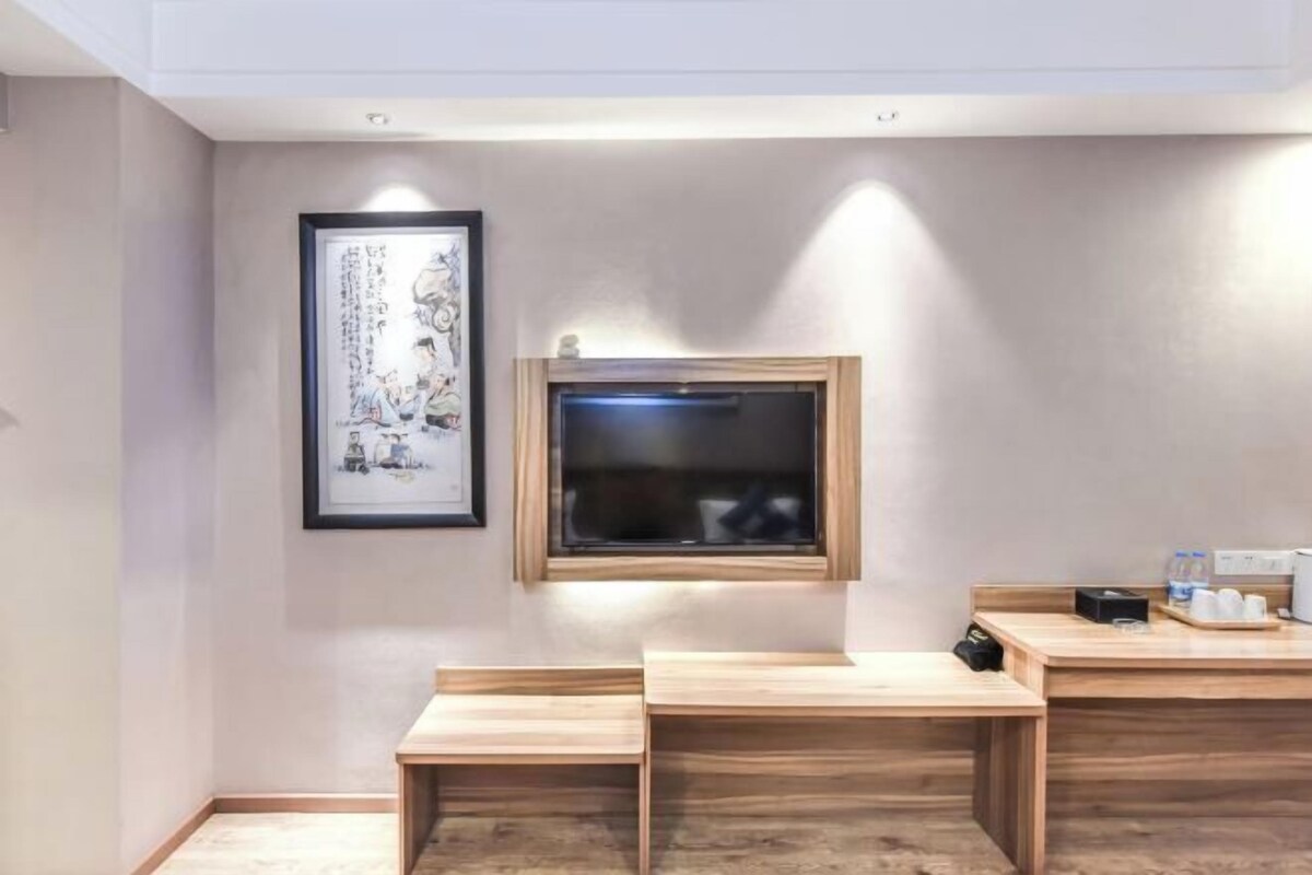 A room with a wooden desk, a framed picture on the wall, and a television mounted above a window.