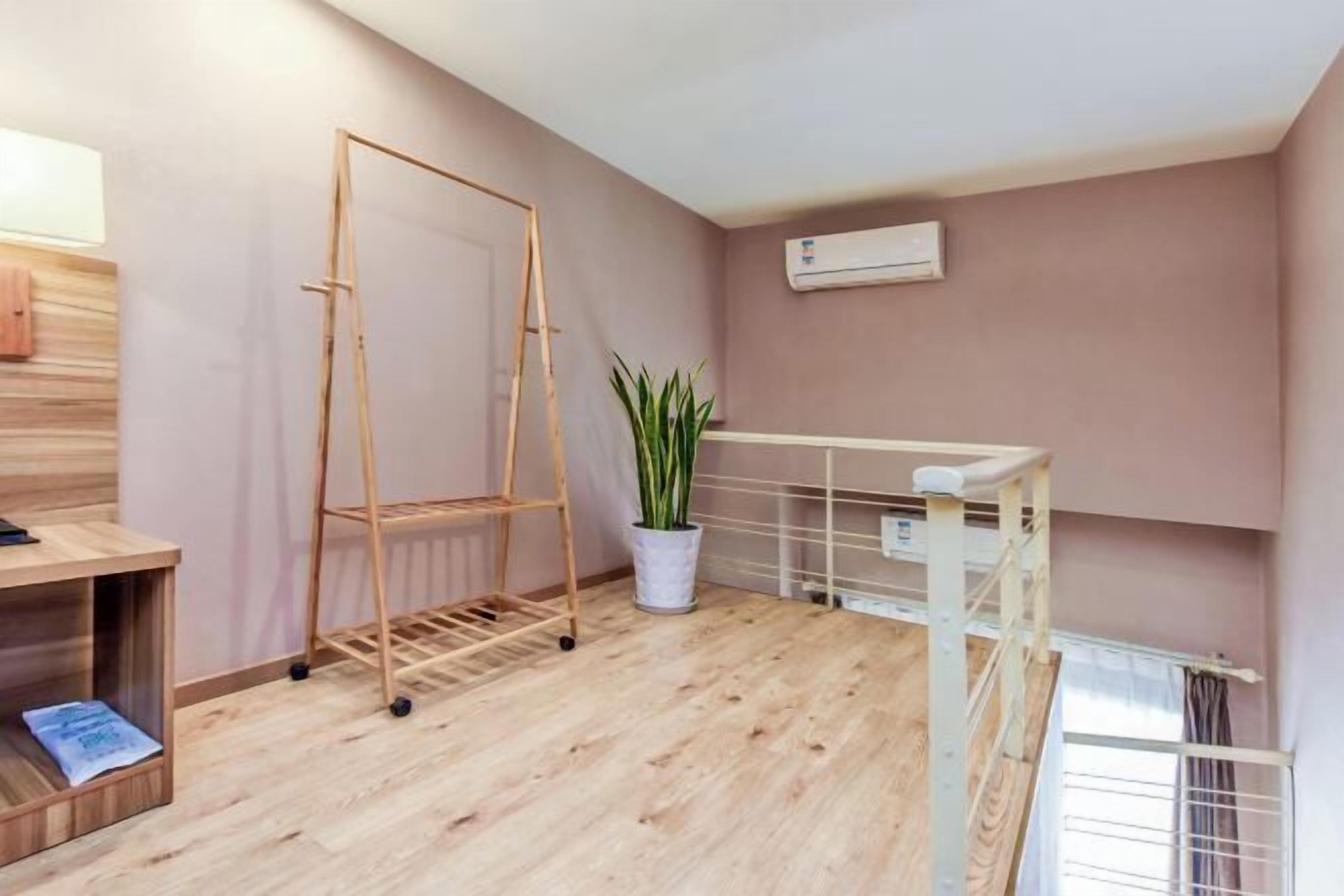 Una habitación con piso de madera, un radiador blanco, una planta en maceta y una escalera metálica blanca.