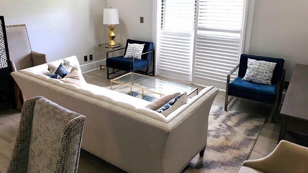 Una sala de estar con un sofá, dos sillones, una mesa de centro, una lámpara y un ventanal con persianas.