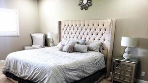 Un dormitorio con una cama grande, dos mesitas de noche, una silla y un reloj de pared.