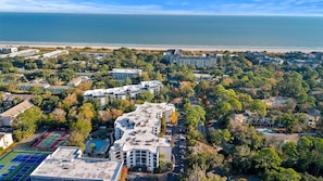 An aerial view of a resort with multiple buildings, a swimming pool, and a beach in the background.