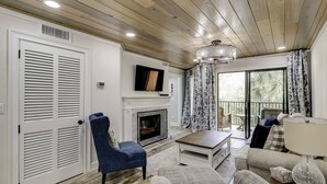 Ein Wohnzimmer mit Kamin, einem darüber hängenden Fernseher und einem Balkon mit Vorhängen.