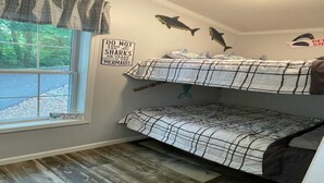 Een slaapkamer met stapelbedden, een raam, een bordje met de tekst 'haaien of zeemeerminnen voeren verboden' en haaienstickers op de muur.