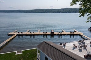 A dock extending into a calm lake with lounge chairs and tables on the dock and on the adjacent grassy area.
