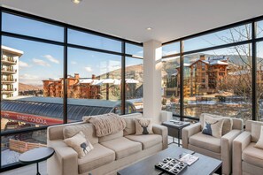 A spacious living area with large windows offering a view of a ski resort and buildings. - 3B lux ski-in/ski-out,gondola,rentals,Peloton bike (Park City)