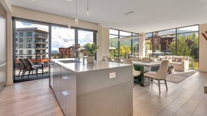Eine moderne Küche mit einer zentralen Kochinsel, großen Fenstern mit Blick auf eine Berglandschaft und einem Essbereich mit einer Couch und Stühlen.