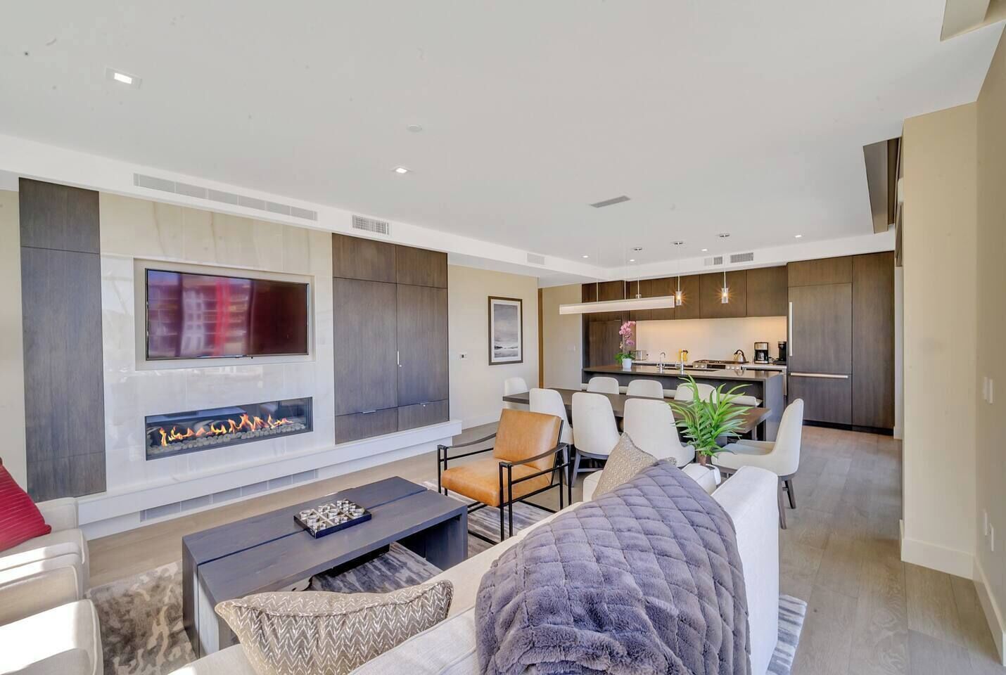 A modern living room with a fireplace, a dining area, and a kitchen.