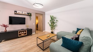 Un salon moderne avec un téléviseur à écran plat, une table basse en bois, un canapé gris et une grande plante en pot.
