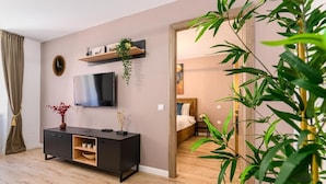 Un salon moderne avec un téléviseur à écran plat, un meuble en bois foncé et une grande plante verte.