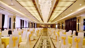 Un salón de banquetes con filas de sillas blancas con cintas amarillas, un pasillo central y una araña.