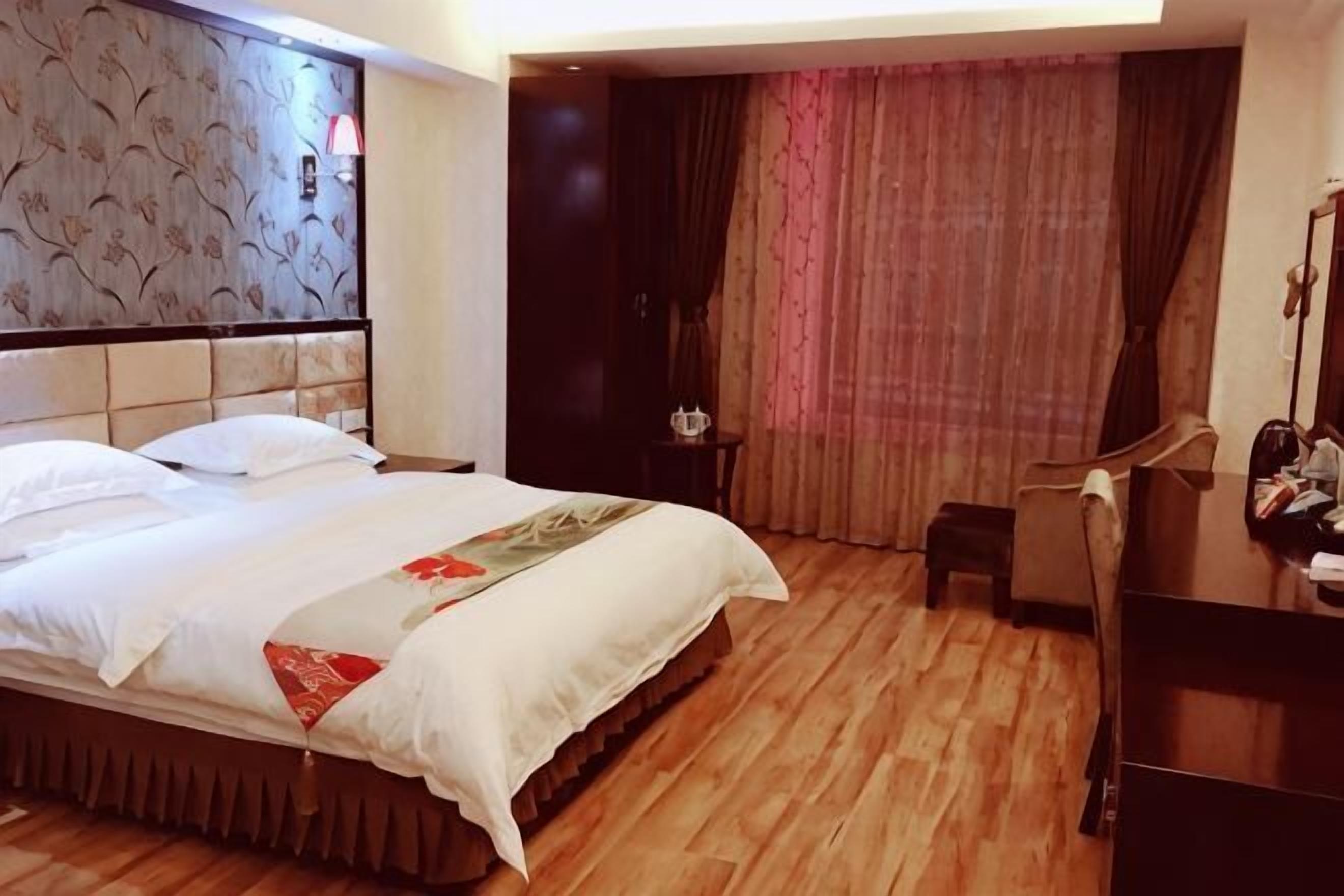 A hotel room with a bed, a small table, a chair, a mirror, and a door leading to another room.