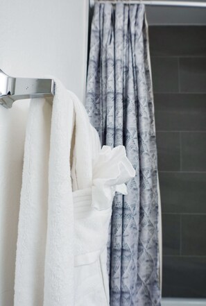 Bathroom features a fluffy towel and a geometric-patterned curtain, tied back to reveal a dark, square-tiled shower area.
