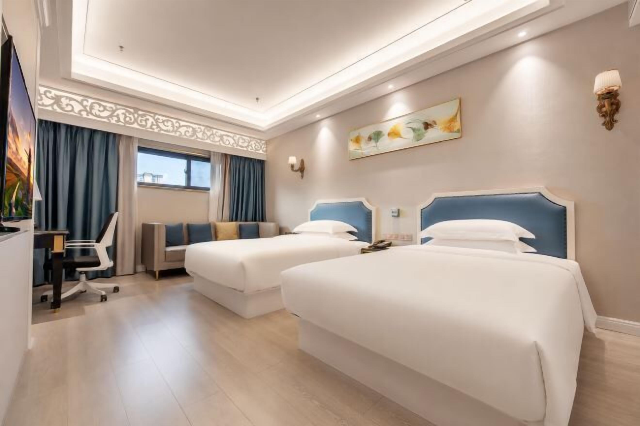 A hotel room with two beds, a desk, a chair, and a TV.