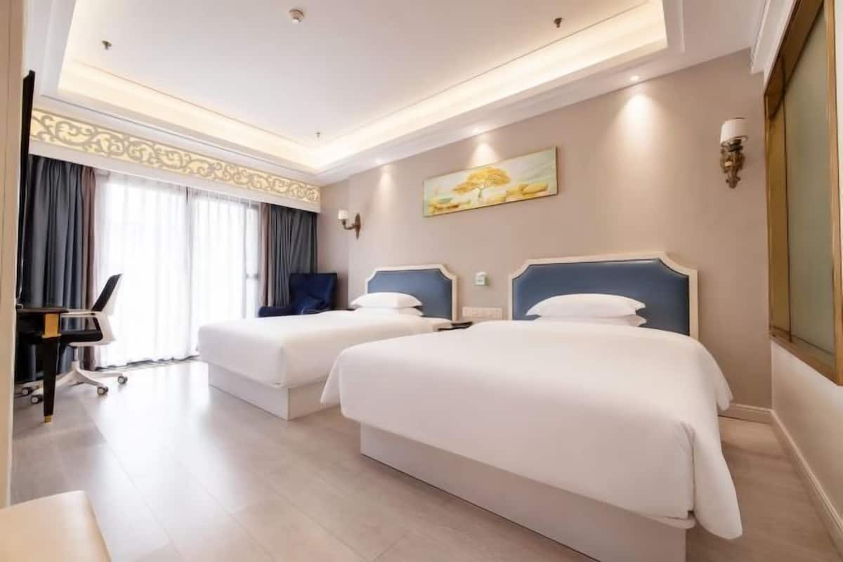 A hotel room with two beds, a desk, and a chair.