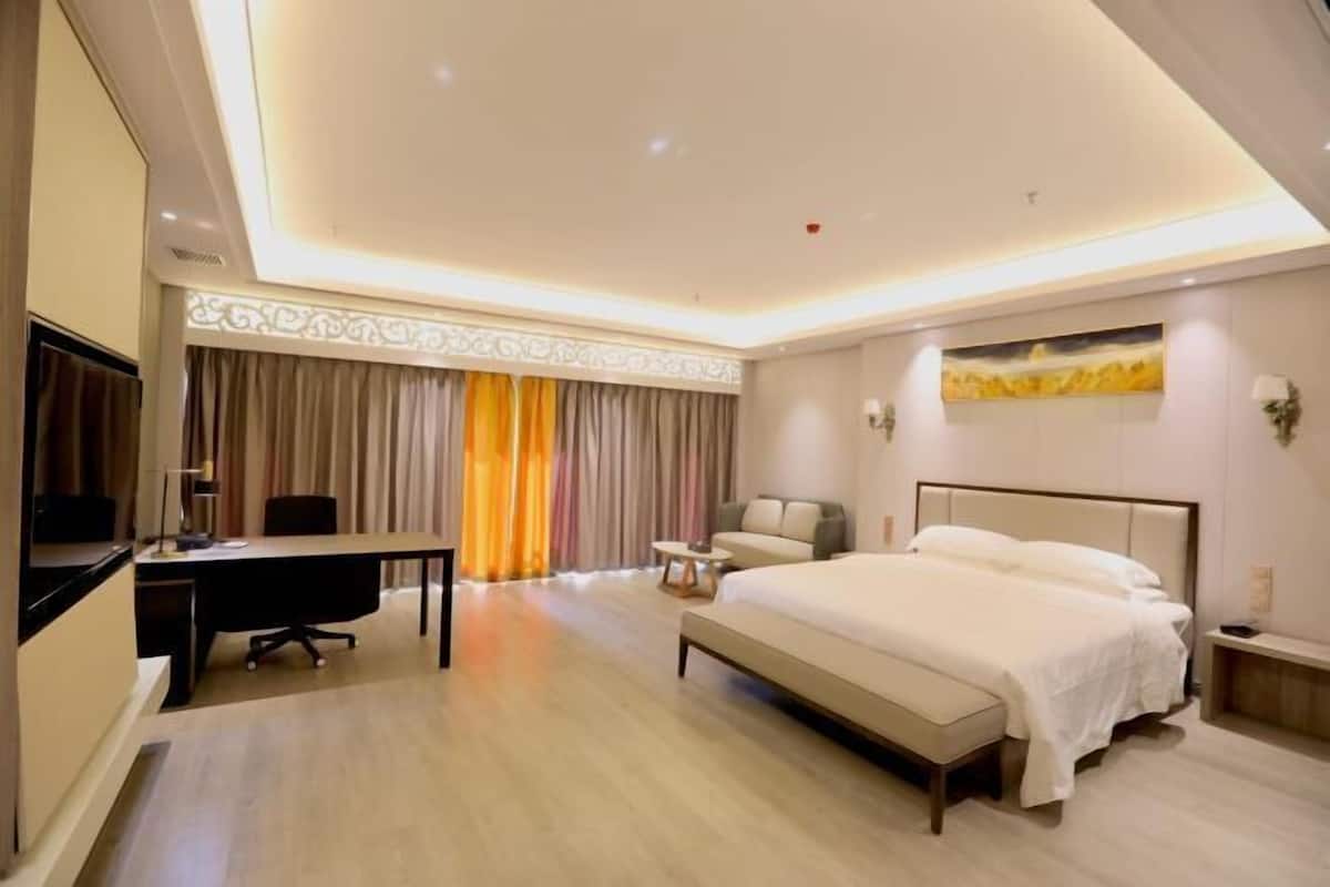 A hotel room with a bed, a desk, a chair, a TV, and a painting on the wall.