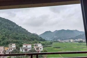 Vista de un paisaje rural con casas y campos, visto a través de una ventana con marco de madera.