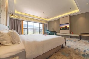 Habitación de hotel con una cama grande, un escritorio, una silla, un televisor y un balcón con vistas.