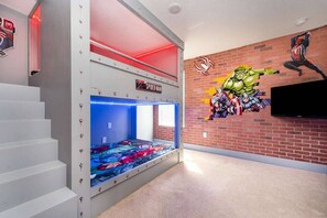 Ein Zimmer mit Etagenbett, einer Wandmalerei von Superhelden und einem Fernseher an der Wand.