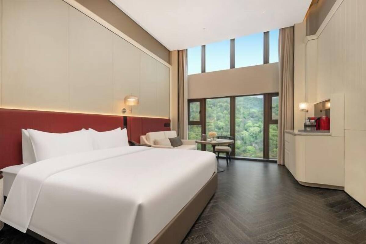 Een hotelkamer met een groot bed, een zithoekje en uitzicht op groen door de ramen.