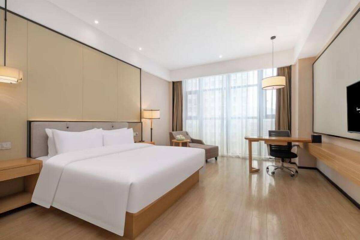 Een hotelkamer met een groot bed, een bureau, een stoel, een televisie en een raam.