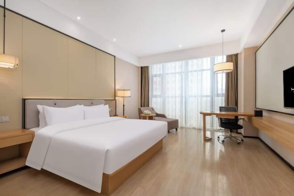 A hotel room with a large bed, a desk, a chair, a TV, and a window.