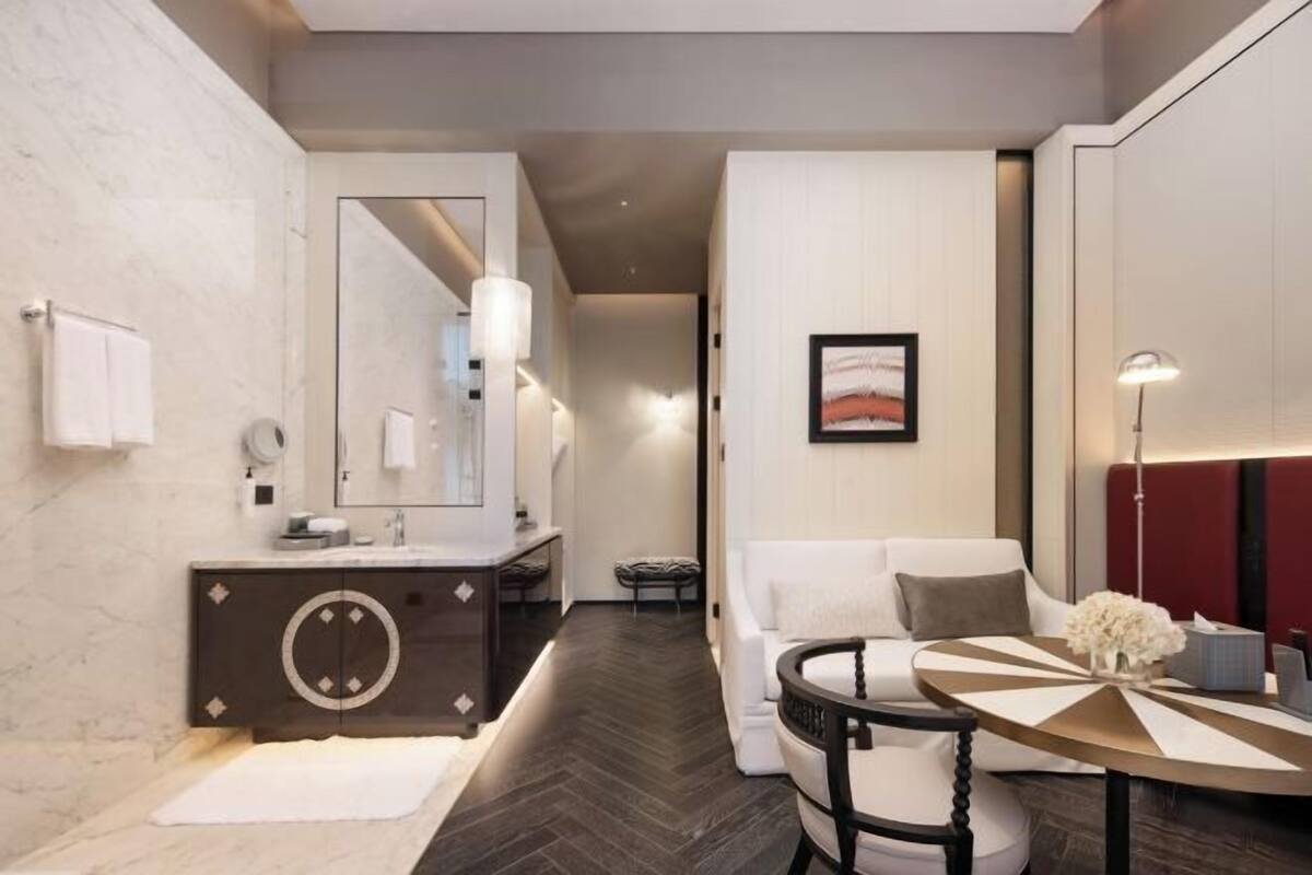 Een moderne hotelkamer met een grote spiegel, een ronde tafel, een bank en een decoratief kunstwerk aan de muur.