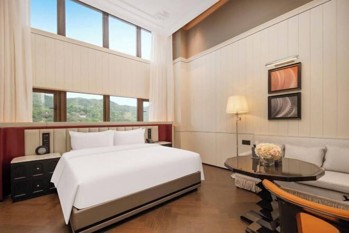 Een hotelkamer met een groot bed, een bank, een tafel met een lamp en uitzicht op groen buiten het raam.