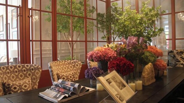 A room with a long table, patterned chairs, a vase of flowers, and a framed picture.