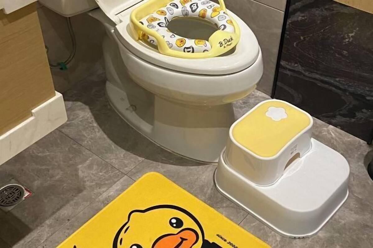 Een toilet met een toiletbril met eendthema en een eendenmat op de vloer.