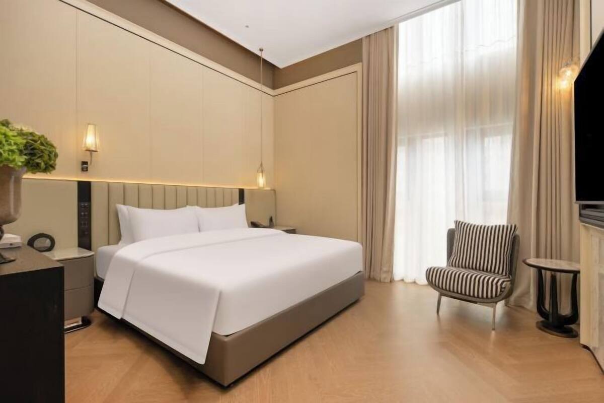 Hotelkamer met een bed, een stoel, een klein tafeltje, een lamp en een televisie.