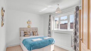 Ein Schlafzimmer mit Bett, Heizkörper, einem Fenster mit Vorhängen und Wanddekorationen.