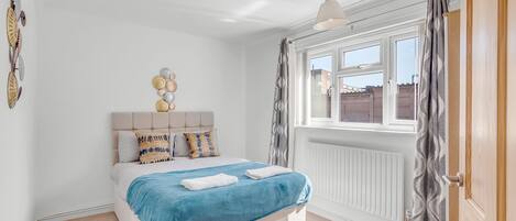 A bedroom with a bed, a radiator, a window with curtains, and wall decorations.