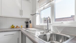 Eine moderne Küche mit weißen Schränken, einer Spüle aus Edelstahl und einem Fenster darüber.
