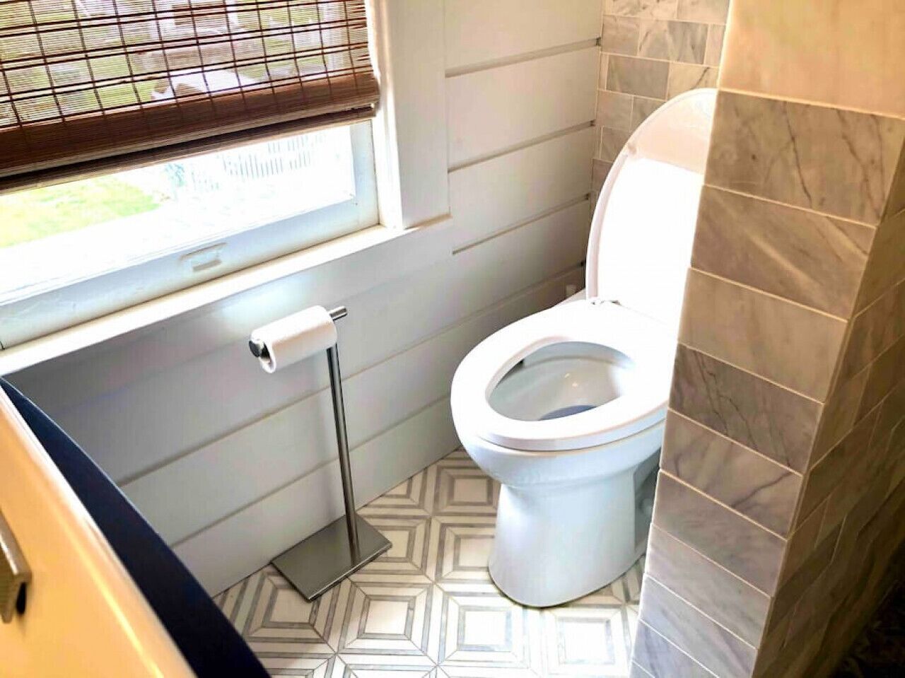 Casa de banho com sanita, suporte para papel higiénico e azulejos de chão estampados.