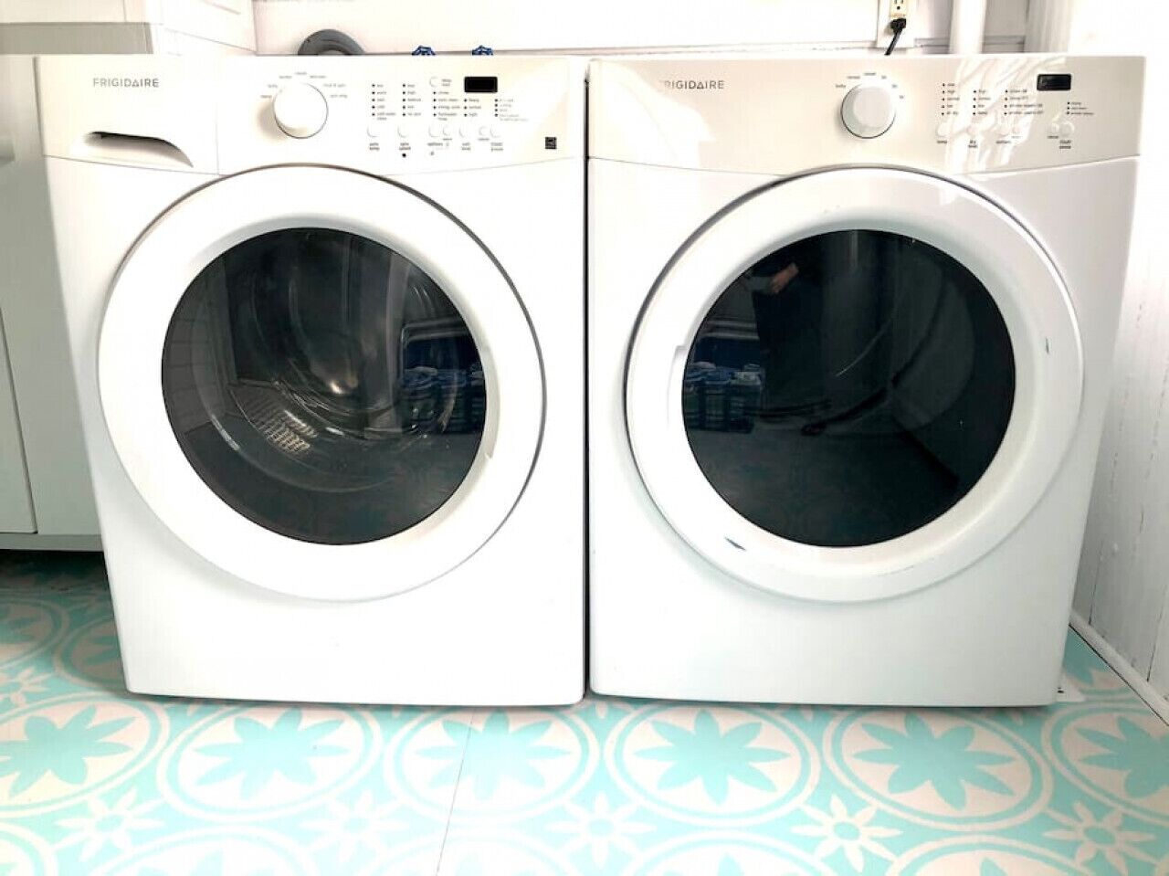 Two white front-loading washing machines with control panels, placed on a patterned floor.