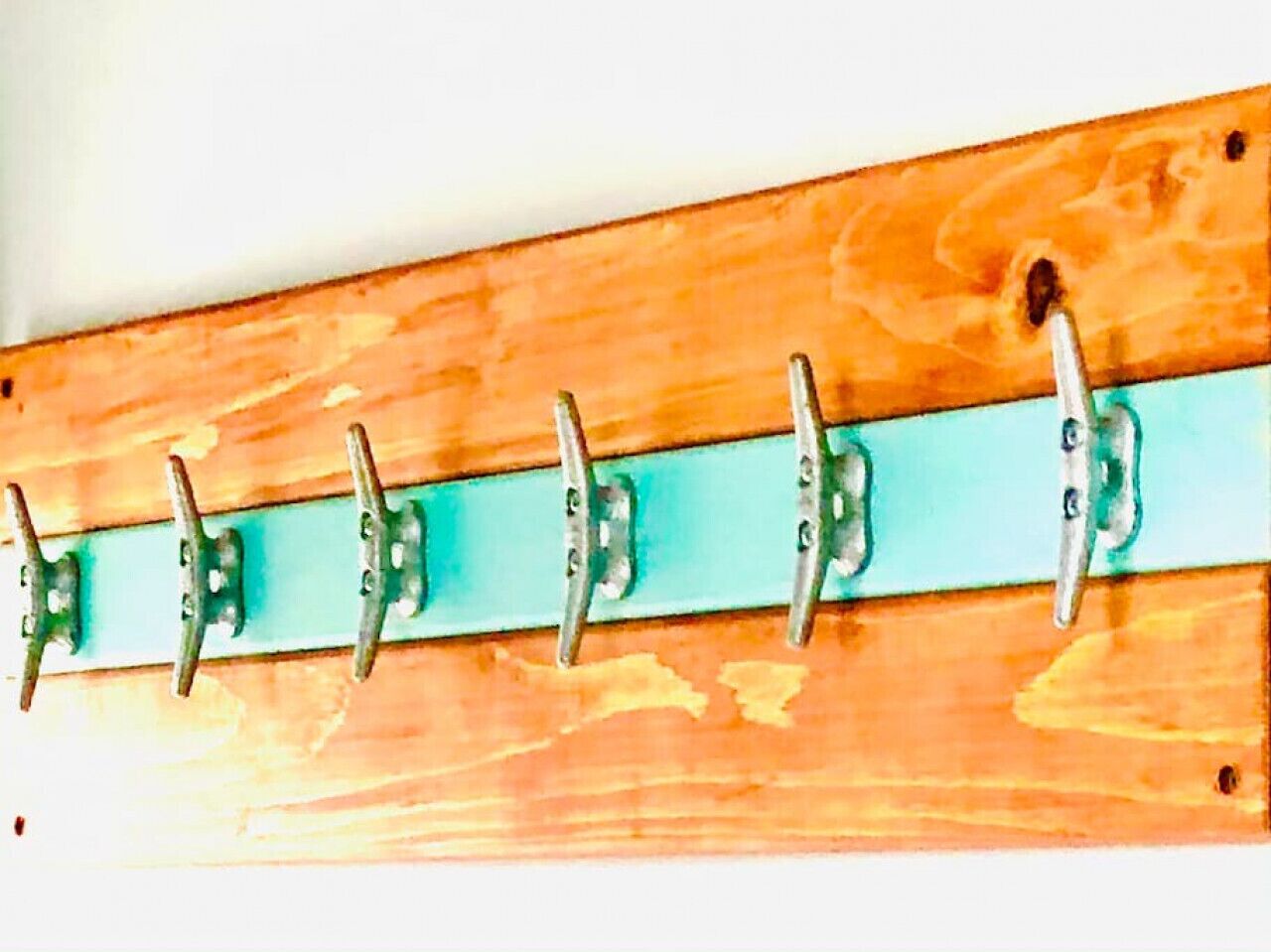 Een houten muur met een horizontaal blauwgroene stang en vijf metalen haken.