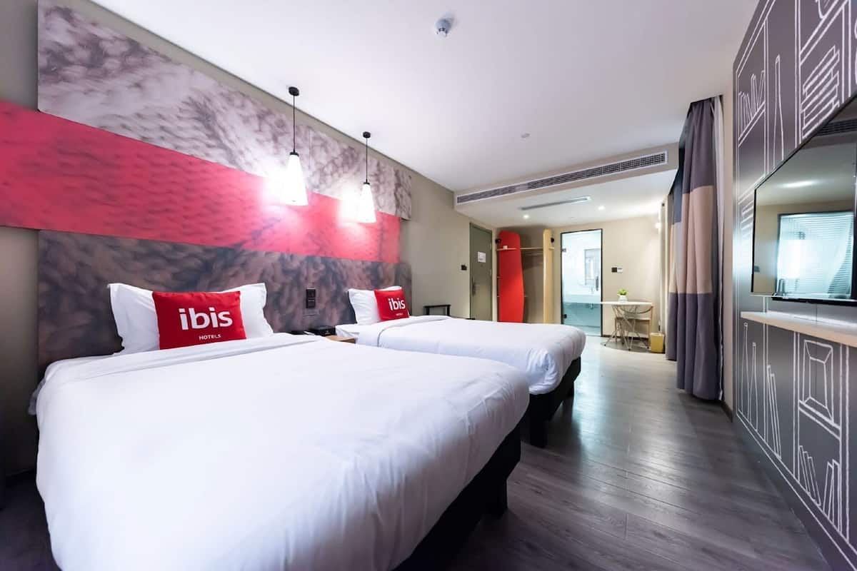 A hotel room with two beds, a TV, a desk, and a bathroom visible through an open door.